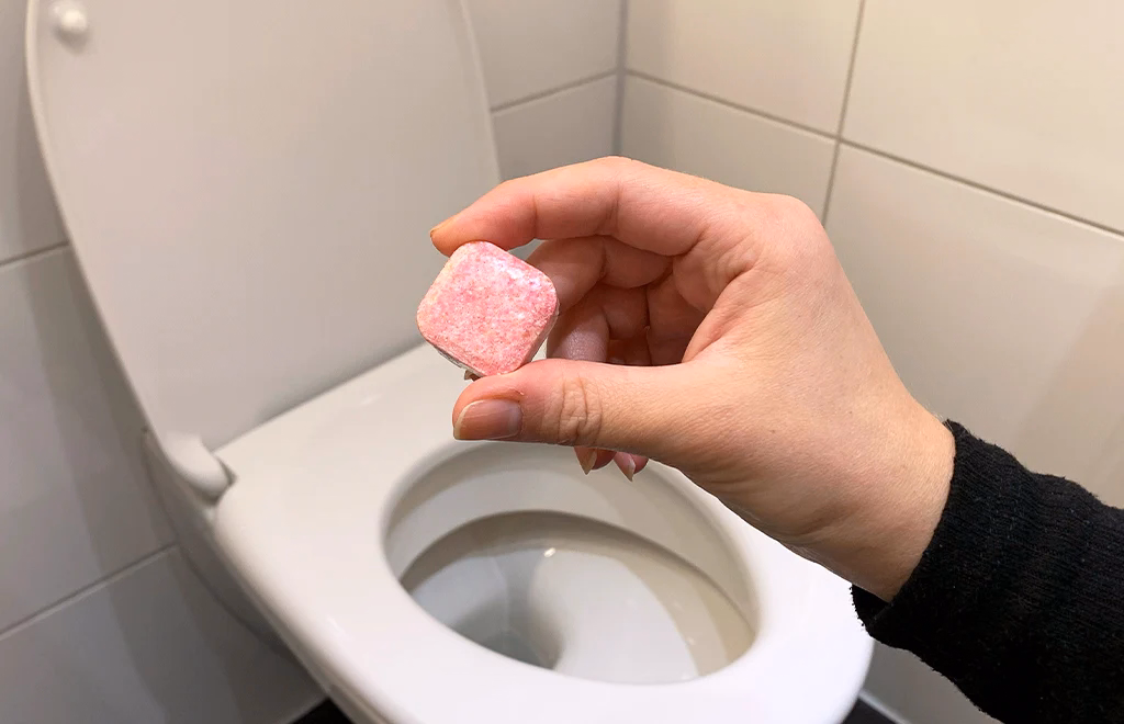 Hand dropping a dishwasher tablet into a toilet bowl