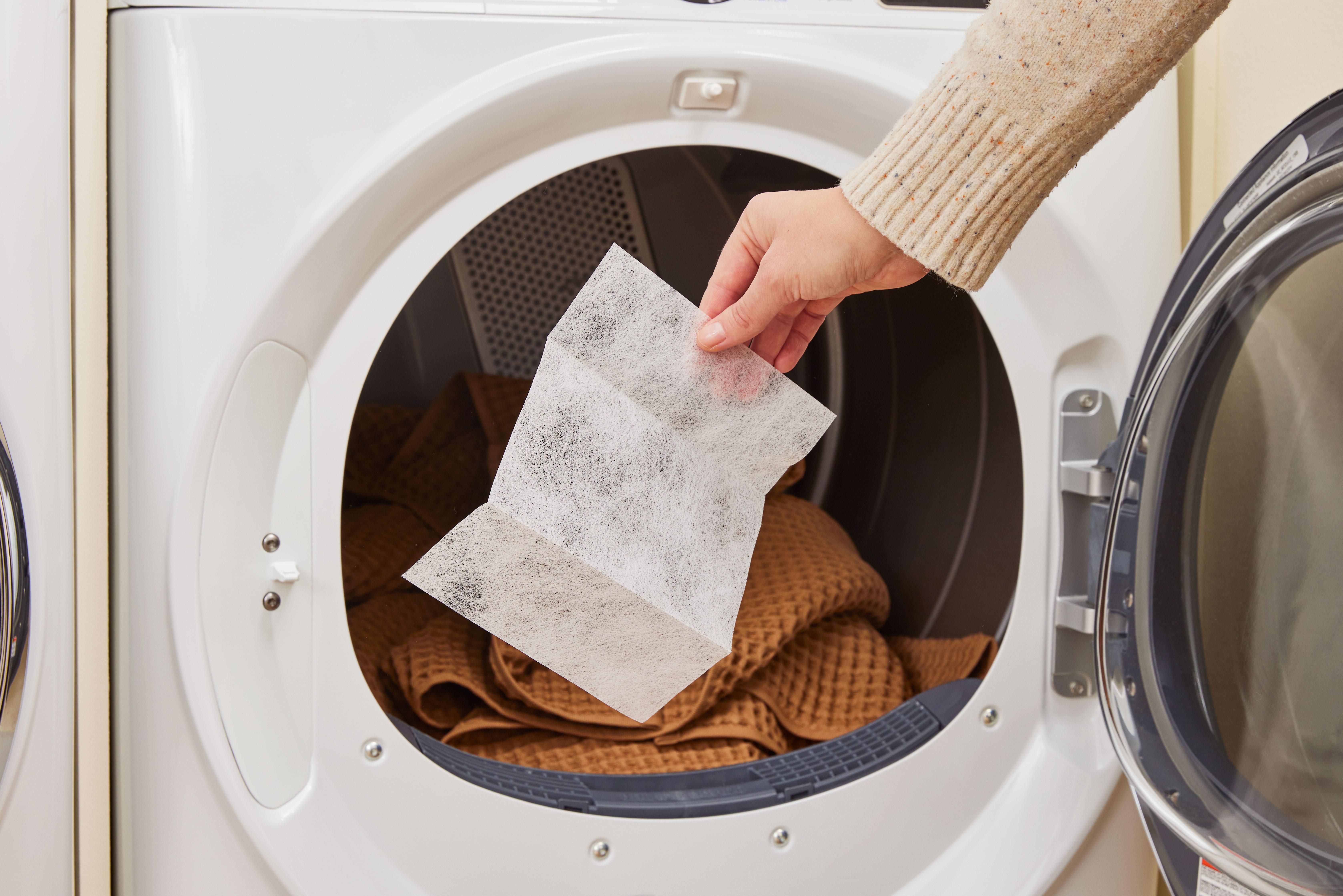 Hand putting a dryer sheet into a tumble dryer